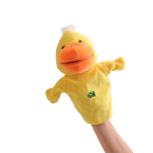 A hand is holding a yellow duck puppet with an orange beak against a white background. The puppet has a small green and black logo on its chest.