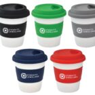 Five reusable coffee cups with lids are displayed. Each cup has a black, green, gray, blue, or red lid and matching sleeve. The logo Eternity Jewellers is printed on each sleeve. The cups are white with a modern, eco-friendly design.