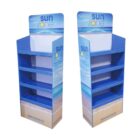 Two blue and white cardboard display stands labeled sun zone with beach imagery. Each has four shelves, designed for retail use. The stands feature a wave and sand graphic on the front.