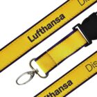 Close-up of a yellow lanyard with Lufthansa printed in black text. The lanyard features a metal clip at one end and a plastic buckle. The background is plain white.