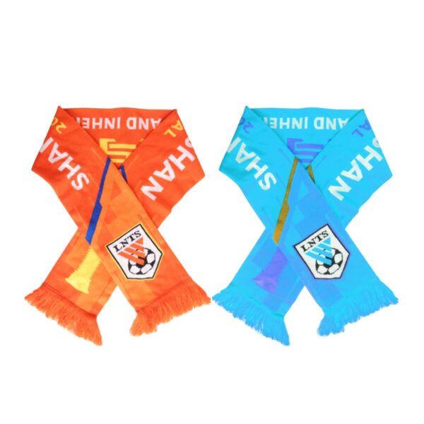 Two crossed soccer scarves, one orange and one sky blue, each featuring the word SHAN and a soccer-themed shield at the center. Both scarves have colorful stripes and fringed ends.