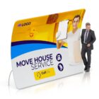 A display banner for a moving service shows a smiling man holding a clipboard and box, with Move House Service written below. Includes icons of moving trucks and a headset, plus a Call Us button. A person in a suit stands beside the banner.