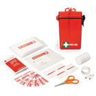 A red first aid kit with a white cross and FIRST AID text is open, displaying contents including bandages, gauze pads, antiseptic wipes, medical tape, scissors, and safety pins, neatly arranged beside it.
