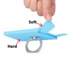 A hand pinches the corner of a light blue phone stand with a metal ring. The stand has a soft, flexible section and a hard base, indicated by text with arrows. The person has glittery nail polish.