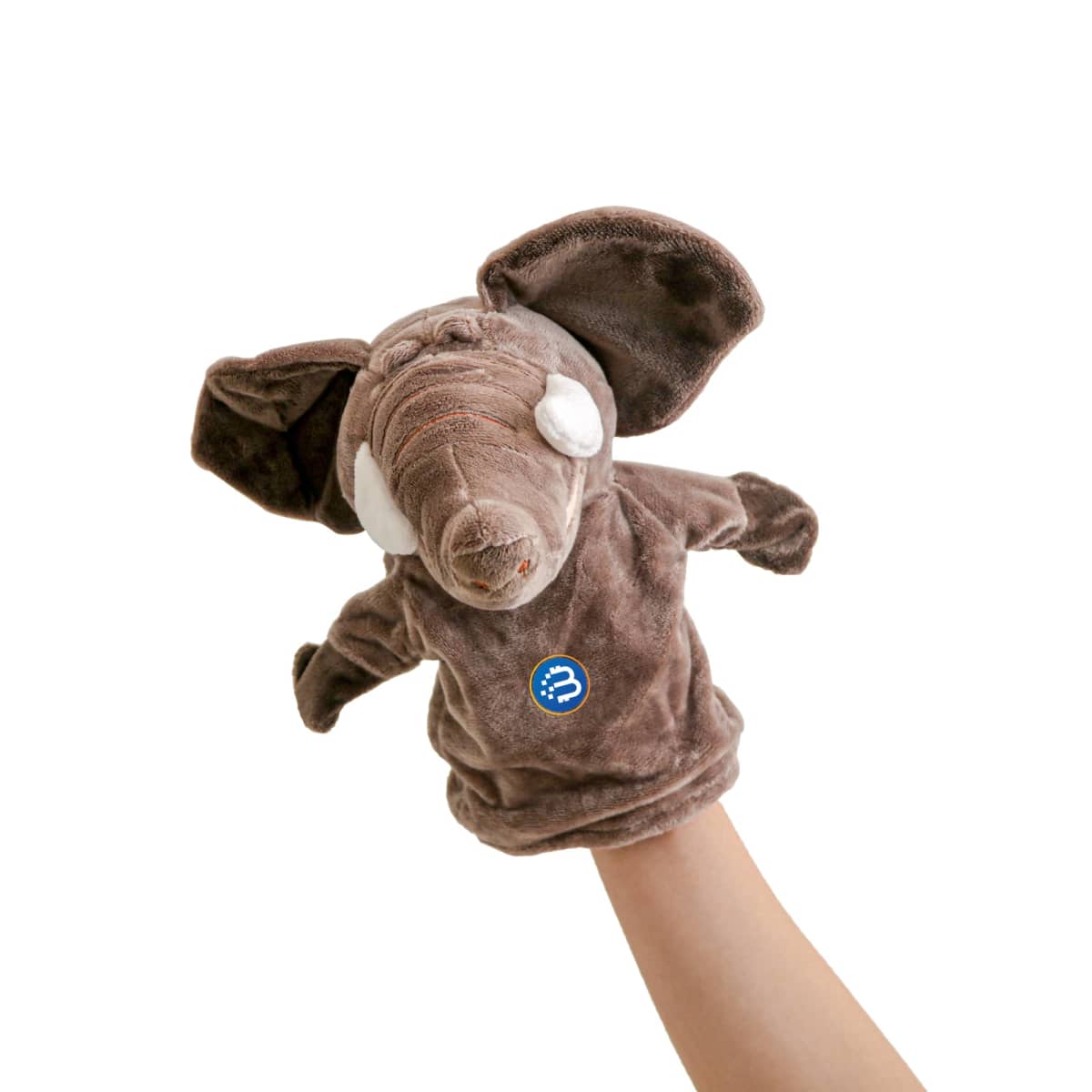 A brown elephant hand puppet with large ears and white eyes is held up by a persons hand against a plain white background. The puppet has a small round patch with a blue logo on its body.