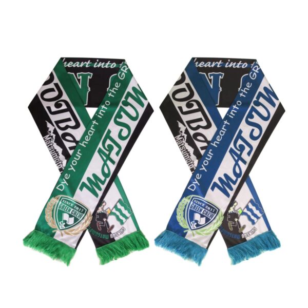 Two soccer scarves, each with Dye your heart into the Green, are displayed. Both scarves show a logo with stripes in green, blue, and white, featuring fringed ends, one with a teal and the other with a light blue tassel.