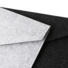 A close-up of two envelopes made from felt material. One envelope is gray and partially overlaps a black one, both positioned diagonally against a neutral background. The texture of the felt is visible.