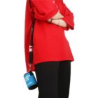 Person in a red shirt with arms crossed, wears a shoulder strap holding a blue portable speaker.