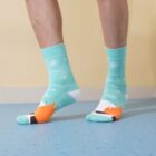 Person wearing teal socks with snowflake patterns and orange flames on the toes, standing on a blue floor against a pale yellow wall.