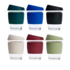 Six reusable glass cups with silicone lids in green, blue, black, cream, red, and olive are arranged in two rows. Each cup has a matching silicone band around the middle.