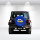 Rear view of a black SUV in a bright, minimalistic garage. The spare tire is covered with a blue cover showing a car wash logo. The vehicle bears the plate “CX130.” Overhead lights illuminate the scene.