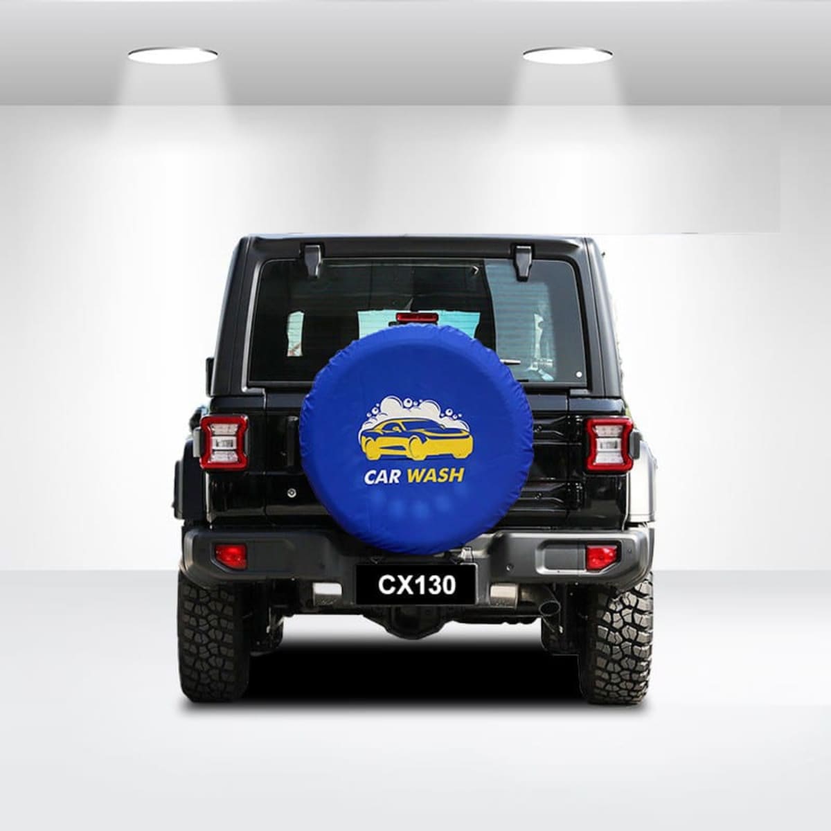 Rear view of a black SUV in a bright, minimalistic garage. The spare tire is covered with a blue cover showing a car wash logo. The vehicle bears the plate “CX130.” Overhead lights illuminate the scene.