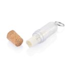 A small, clear capsule with a removable cork lid lies on a white surface. Inside the capsule, a rolled paper with visible text is partially unrolled. A metal clasp is attached to the capsule.