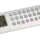 A silver multifunctional digital ruler featuring a calculator and clock on the top surface. The ruler has a numerical keypad, various function buttons, and a small digital display showing the time and date.