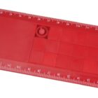 A red plastic ruler with 15 centimeters marked in white along the top and bottom edges. It features a grid with small, square compartments and a circular indentation near the center.