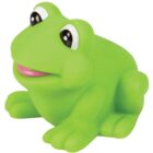A green rubber frog toy with large, shiny eyes and a pink mouth sits upright. The frog has a smooth texture and simple design, giving it a playful, cartoon-like appearance.