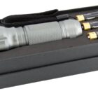 A silver flashlight with a textured grip and wrist strap is placed in an open black box. Three AA batteries are lined up next to it inside the box.