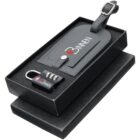 Black travel accessory gift set including a leather luggage tag with a buckle and a combination lock, both with a logo, presented in a foam-lined black box.