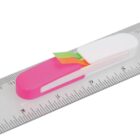 A silver ruler marked with metric measurements has a white and pink dispenser attached to it, holding small, colorful sticky notes in green and yellow.