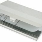 A silver business card holder with a textured lid is partially open, revealing a stack of business cards inside. The design is sleek and minimalist.
