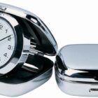 A shiny chrome travel alarm clock, partially open with a white face and black numerals, sits next to its closed metallic cover. The clocks hands point to approximately 10:10.