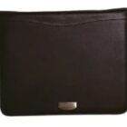 A dark brown, rectangular leather laptop sleeve with a smooth texture. It has a subtle curved stitch near the top and a small metallic logo plate at the bottom center.