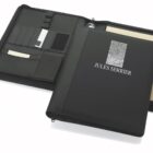 Open black leather portfolio with Jules Serrier and a fingerprint design on the cover. The interior features organized slots for cards, a pen holder, a notepad, and a section for loose papers.