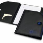 Open black portfolio folder with three sections: a slot for sticky notes, a legal pad on the right, and a closed section in the center. The folder has a blue accent with a snap button closure and embossed text on the front.