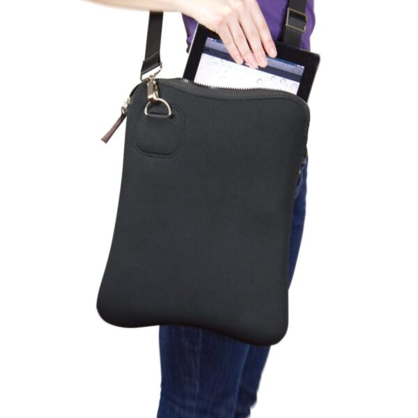 A person in a purple shirt and jeans is holding a black shoulder bag with one hand. They are placing or removing a tablet from the zippered main compartment of the bag.