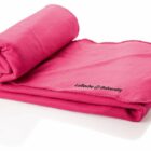 A bright pink blanket is partially rolled up on a white surface. It features the embroidered text La Roche University in black on one corner.