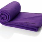 A purple fleece blanket is rolled up, with a portion unrolled showing LaRoche University embroidered in black. The edges have decorative stitching. The blanket is set against a plain white background.
