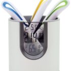 A digital thermometer holder with a display showing 21.4°C and 65.1°F. It contains three thermometers with colorful handles: blue, yellow, and green. The holder is predominantly gray and white.