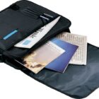 Open black messenger bag with a shoulder strap, containing a newspaper, a magazine, and a pen. The flap is fully open, and other papers are visible inside. The bag is resting against a white background.