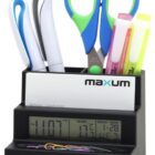 A black desk organizer holding blue and green scissors, pens, highlighters, and a business card. The base features a digital clock displaying time, temperature, and date, with colorful paperclips arranged in front.