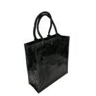 A glossy black tote bag with a rectangular shape and smooth surface. It has two black handles and appears to be made from a shiny, possibly leather-like material. The interior is visible at the top.