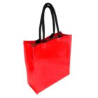 A red, glossy tote bag with black handles is standing upright. The bag has a shiny, smooth surface and a rectangular shape, designed for carrying items. The handles are long enough to be carried over the shoulder.