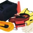 An emergency car kit with a black bag, jumper cables, yellow tow rope, first aid kit, flashlight, safety vest, orange cone, gloves, and a plastic bag.