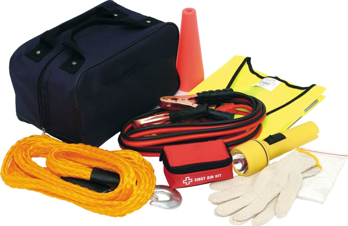 An emergency car kit with a black bag, jumper cables, yellow tow rope, first aid kit, flashlight, safety vest, orange cone, gloves, and a plastic bag.