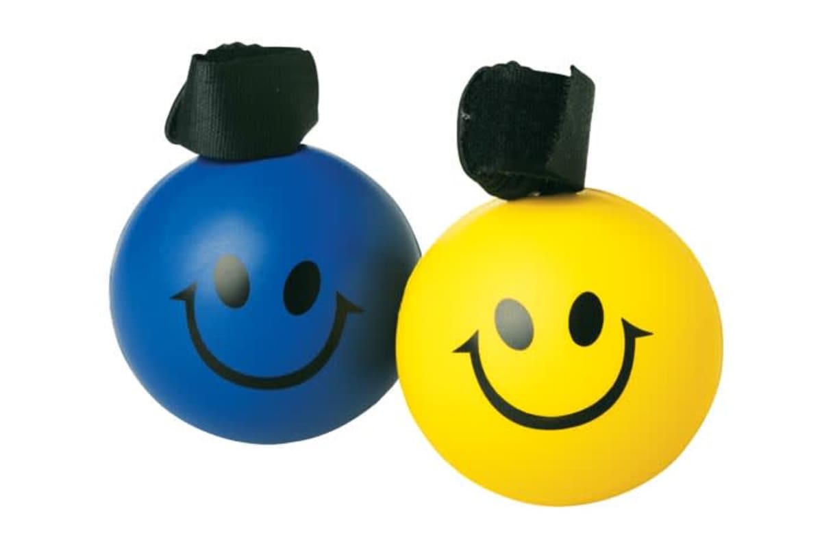 Two round stress balls with smiling faces, one blue and one yellow, each with a black strap on top, resting against each other on a plain white background.