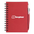 A red spiral-bound notebook with a white berghaus logo on the cover. A black pen is attached to the right side.