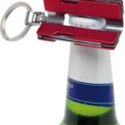 A red bottle opener attached to a keyring is shown in action, opening a bottle with a white cap and blue label. The opener is positioned at the top of the bottle, ready to remove the cap.