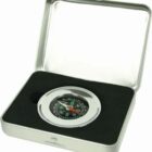 A silver compass with a black face displaying cardinal directions is set in a foam-lined metal case. The compass needle is pointing towards north. The case is open and has a hinged lid.