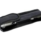 A metallic flashlight partially inside a black fabric case with a Velcro flap. The case has a textured surface and stitching along the edges. The flashlights silver head and knurled grip are visible.
