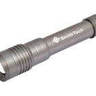 A metallic flashlight with a ribbed grip is positioned diagonally against a white background. SmithTech is printed on the side in white lettering.