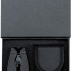 A black multi-tool and a matching black carrying pouch are neatly placed in a black foam-lined box. The multi-tool is folded, and the box lid is open, showing the contents clearly.