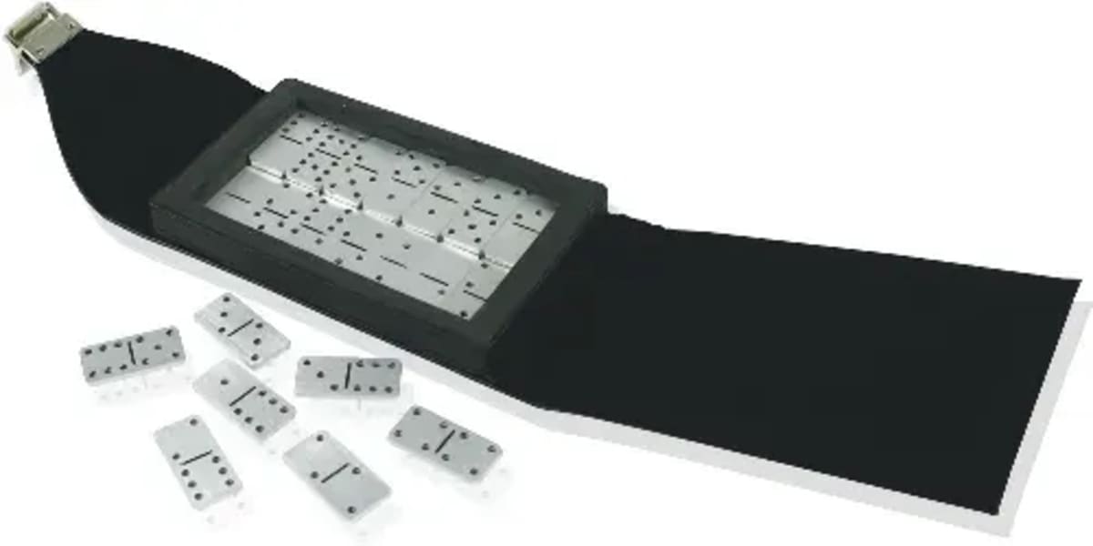 A black wristwatch designed to resemble a domino set, with a rectangular face showing domino dots. Several small dominos are scattered alongside the unbuckled black strap.