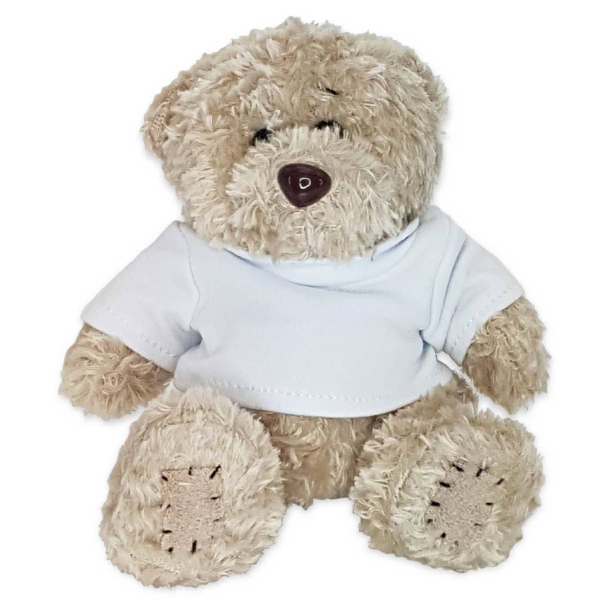 A soft, brown teddy bear is seated, wearing a white T-shirt. The bear has fluffy fur and a dark brown nose, giving it a cute and cuddly appearance. Its legs and arms are slightly spread out in a relaxed pose.