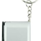 A small, rectangular silver gadget with a black button on the side, attached to a metal keychain. The device is compact and minimalist in design.