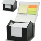 A black and gray desk organizer resembling a house, containing white note papers inside and sticky notes in yellow, orange, and green on the lid. The organizer is shown both closed in the background and open in the foreground.