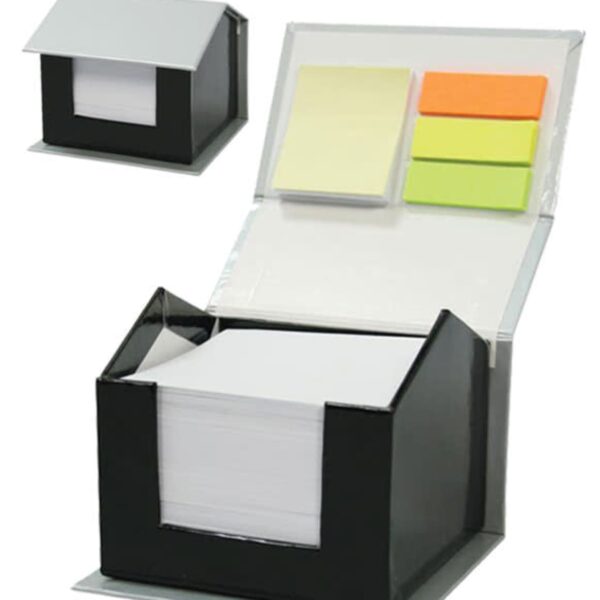 A photo showing a black cube-shaped holder with a slanted lid, resembling a small house, holding white notepaper. Nearby, the lid is open, revealing sticky notes in pastel colors—yellow, orange, and green—inside the lid.